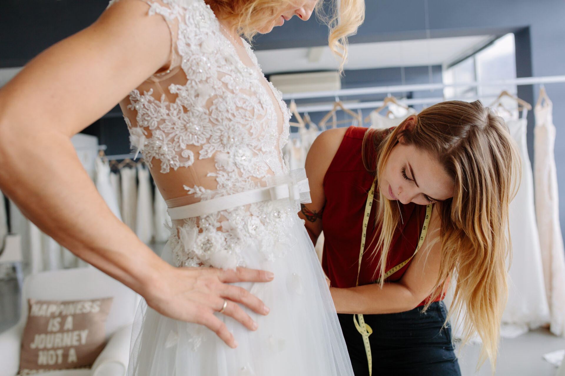 Skillful dress designer fitting wedding gown to woman in her boutique. Woman making adjustments to bridal gown in fashion designer studio.